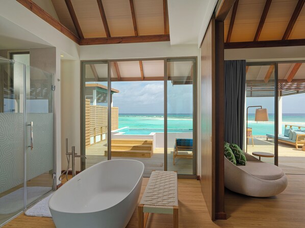 A modern bathroom with a freestanding bathtub, a glass-enclosed shower, and a view of the ocean.