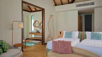A hotel room with a wooden floor, a bed with white bedding, a sofa with green and pink pillows, a small round table, and a mirror with a wooden frame.