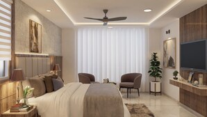 Un dormitorio moderno con una cama grande, dos sillones, un televisor y un ventilador de techo.