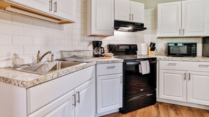 A modern kitchen with white cabinets, a stainless steel sink, a black stove, and a microwave.
