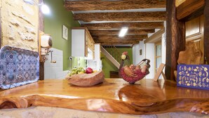 Ein rustikaler Innenraum mit Holztisch, Steinwand und einer Treppe, die in ein Obergeschoss führt.