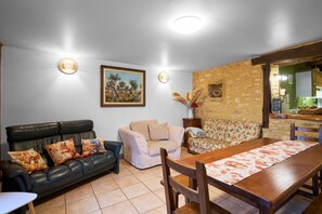A living room with a sofa, a dining table, and a kitchen area visible through an open doorway.
