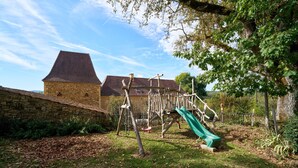 Ein Spielplatz mit Rutsche und Schaukeln, eine Steinsäule und ein Gebäude mit geneigtem Dach.