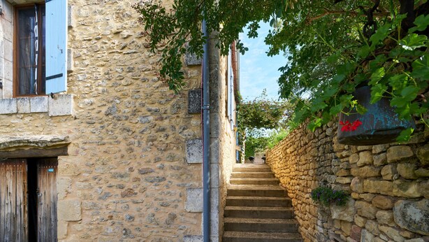 Eine schmale Steintreppe führt zu einem Gebäude mit einer Holztür und einem Fenster mit blauen Rollläden.
