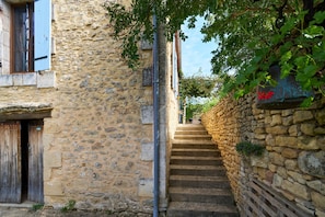 A narrow stone staircase leading up to a building with a wooden door and a window with blue shutters.