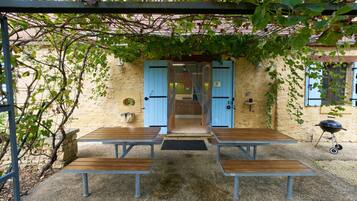 An outdoor seating area with tables and benches, a pergola, and a building entrance with blue doors.