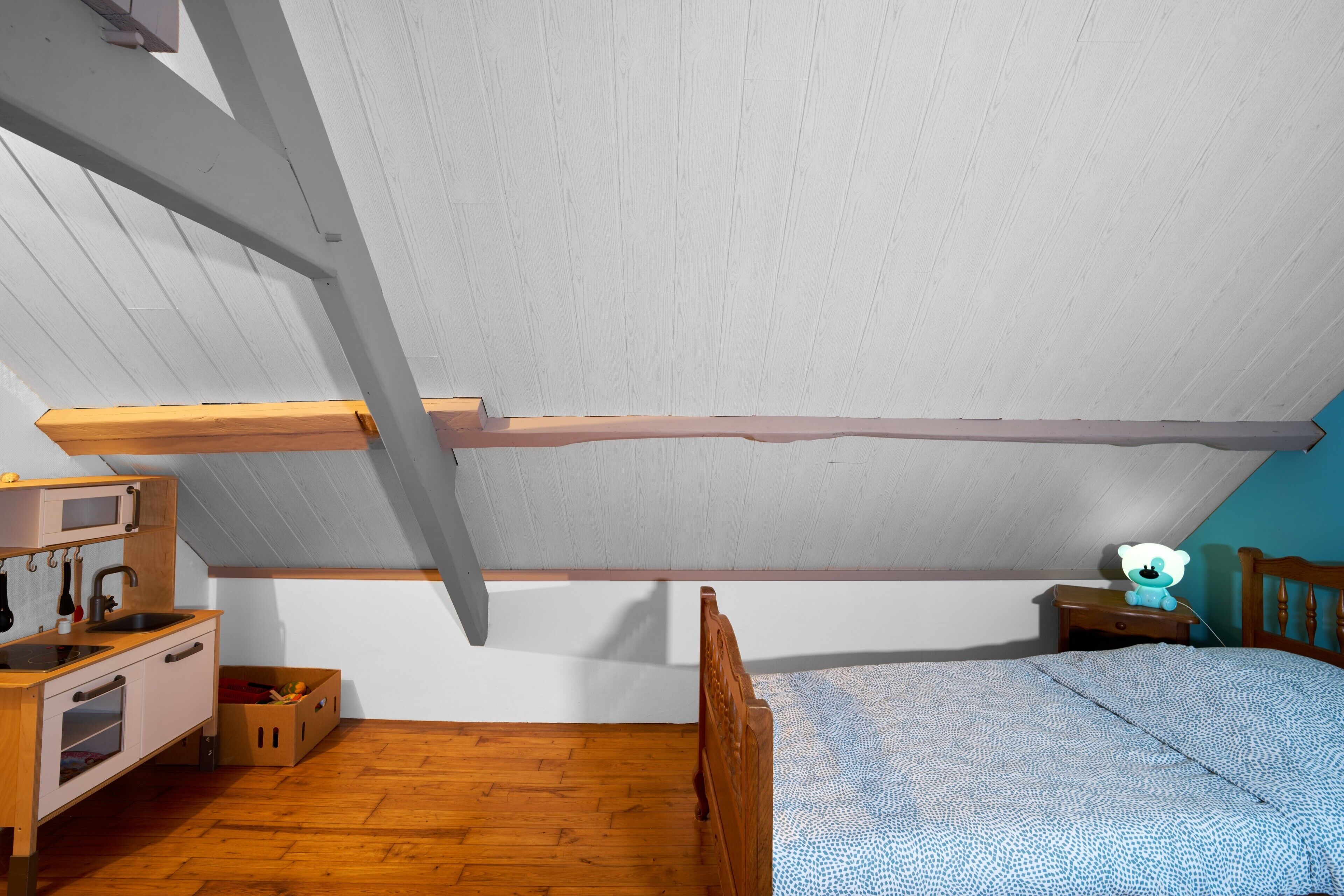 Ein Schlafzimmer mit schrägem Dach, Holzmöbeln, einem Bett, einem Nachttisch und einer kleinen Kommode.