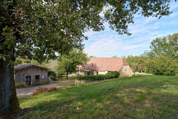 A rustic house with a sloped roof, surrounded by a grassy area and trees.