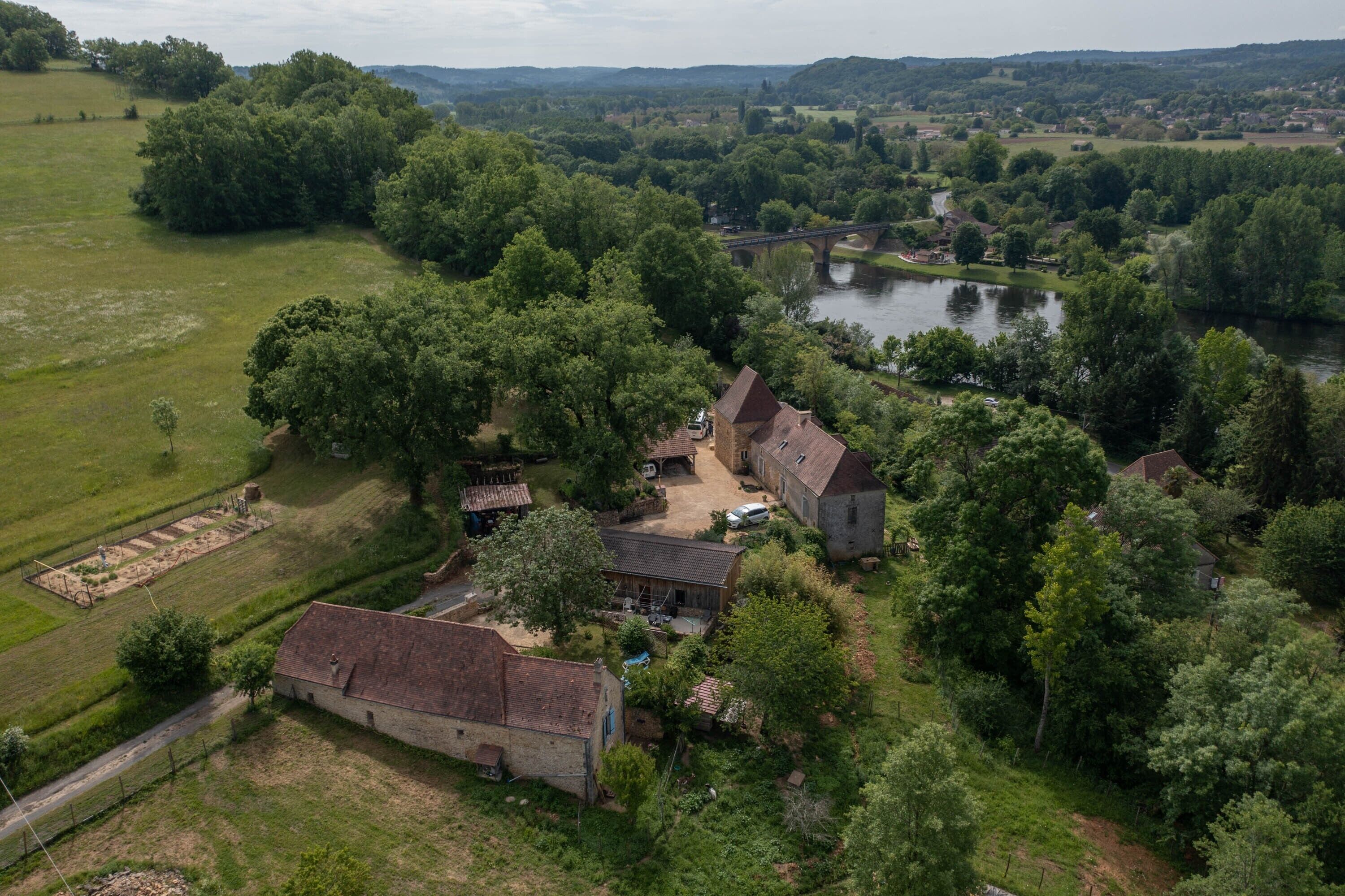 Une vue aérienne d’une zone rurale avec une rivière, un pont et plusieurs bâtiments entourés de verdure.