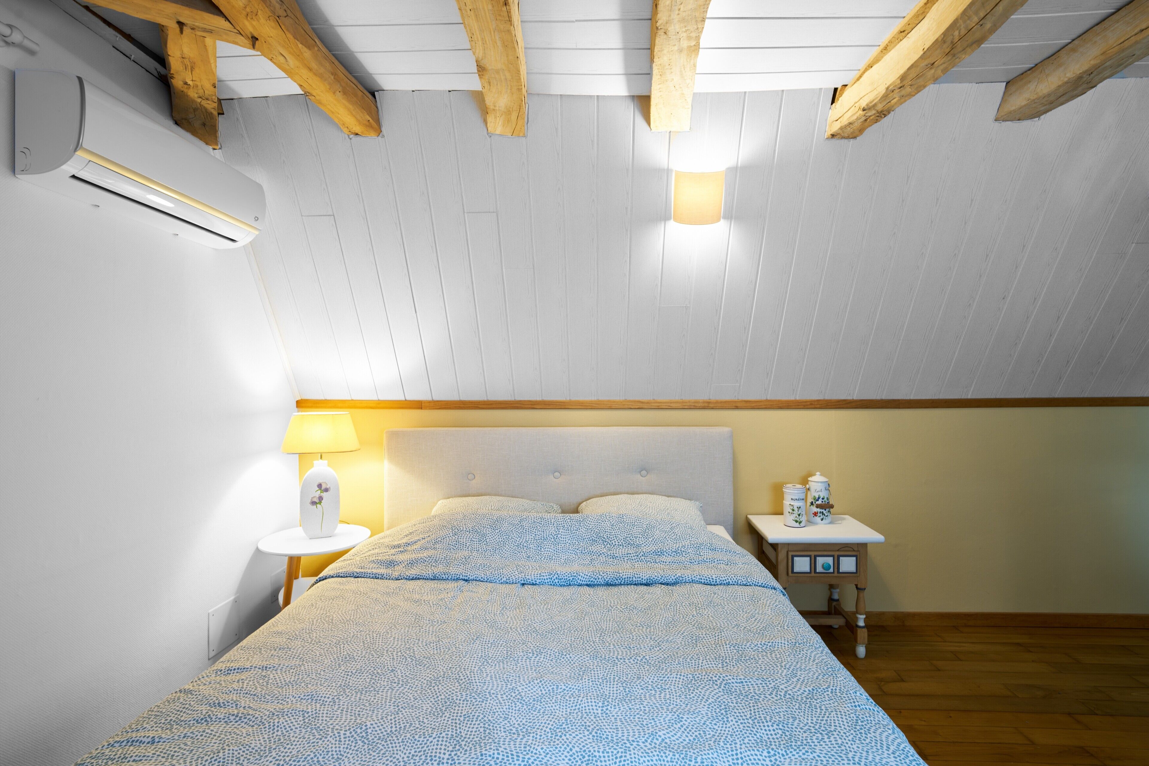 A bedroom with a bed, bedside table, lamp, and an air conditioning unit.