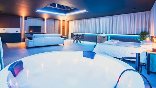 Ein modernes Hotelzimmer mit einer großen runden Whirlwanne, einem Sofa, einem Bett und einem Fernseher.