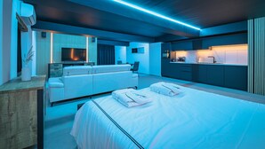 A modern hotel room with a bed, a sofa, a TV, and a kitchenette.