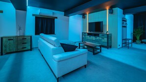A modern living room with a sofa, a coffee table, and a TV. There is a wooden cabinet and a plant.