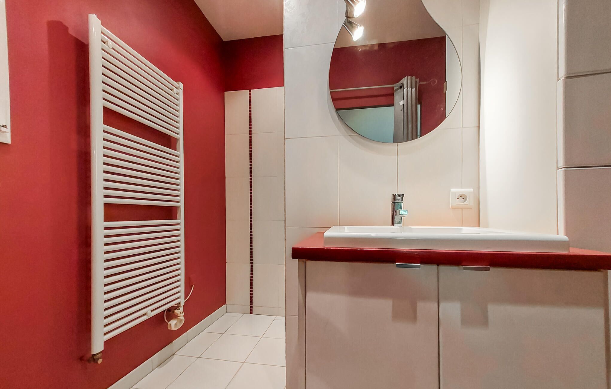 Un baño con pared roja, radiador blanco, lavabo y espejo.