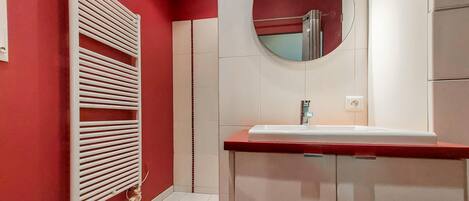 Un baño con pared roja, radiador blanco, lavabo y espejo.
