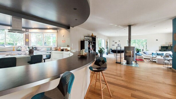 A modern kitchen with a curved island, bar stools, and a large window. - 3 bedroom nice home in Sarliac (Sarliac)