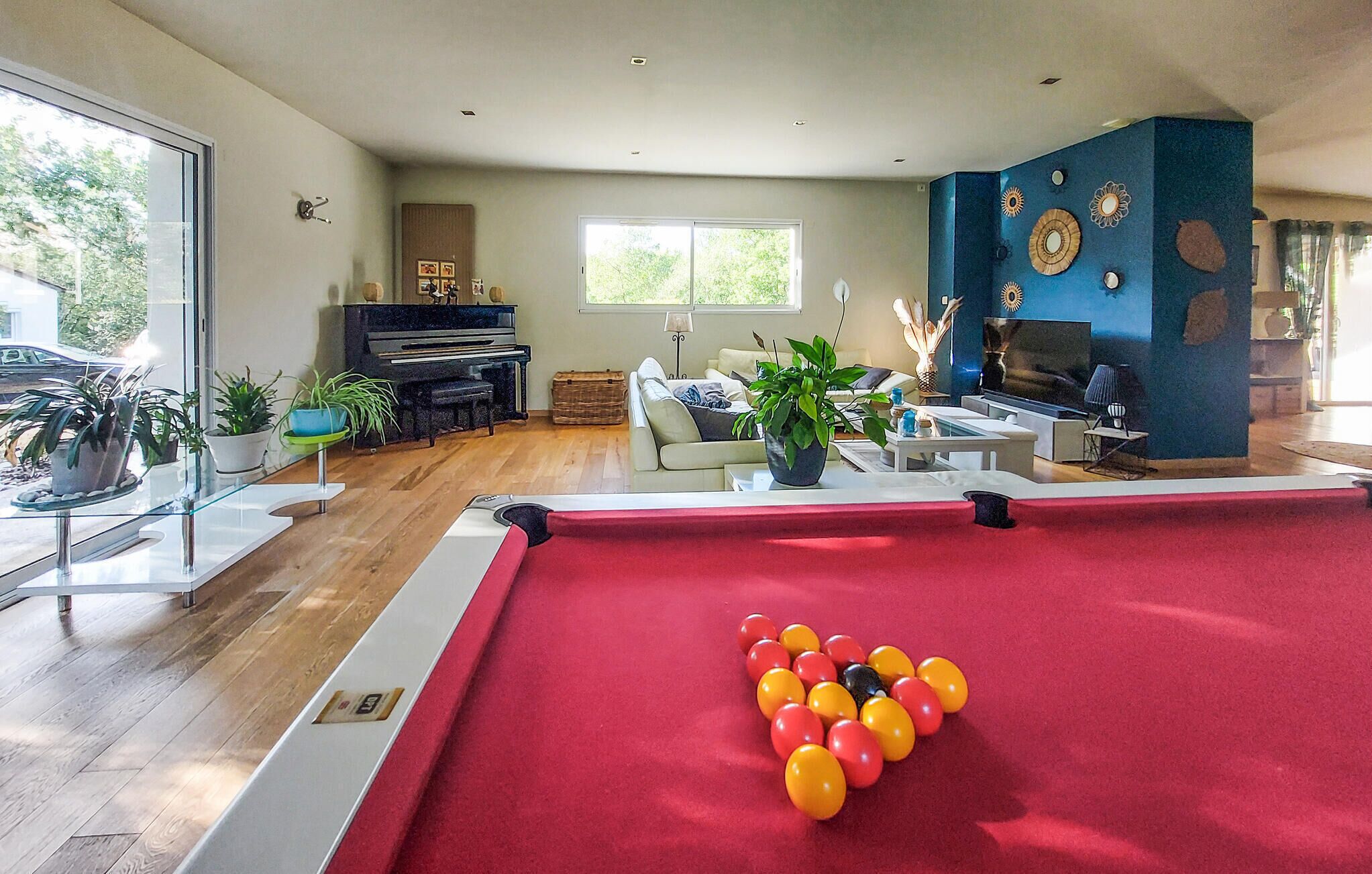 Uma sala de estar ampla com mesa de bilhar, piano e televisão.