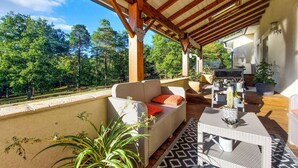 A covered outdoor seating area with wicker furniture, potted plants, and a view of a forested area. - 3 bedroom nice home in Sarliac (Sarliac)