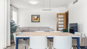 A modern living room with a wooden dining table, white chairs, a grey sofa, a TV, and a painting on the wall. - NEW! Ciudad de las Artes Apartment (València)