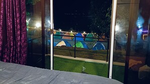 Ein Zimmer mit einem Bett, einem Fenster mit Blick auf bunte Zelte draußen und einem Vorhang links.