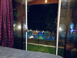 Quarto com uma cama, uma janela com vista para tendas coloridas do lado de fora e uma cortina à esquerda.