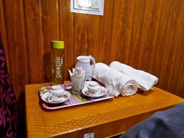 Uma mesa de madeira com uma bandeja contendo uma garrafa de água, um jarro, um bule, xícaras, pires e uma toalha enrolada.