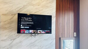 Ein modernes Zimmer mit Marmorwand, einem an der Wand befestigten Fernseher, der eine Speisekarte zeigt, einem Holztisch mit Wasserkocher, einem Stuhl und einem Fenster mit Aussicht.