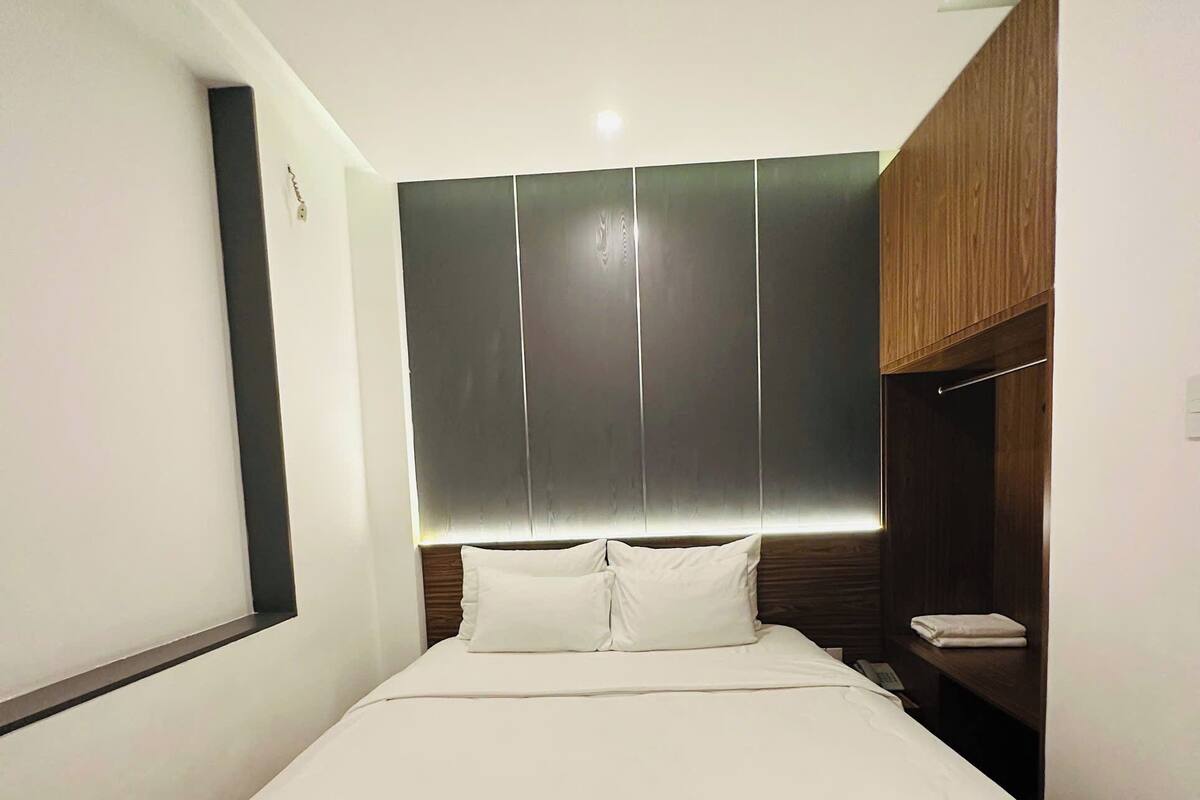 A modern hotel room with a large bed, a wooden headboard, and a built-in shelf.