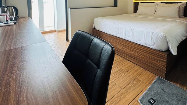 Ein Hotelzimmer mit einem Holztisch, einem einzelnen schwarzen Stuhl, einem Bett mit weißer Bettwäsche und einem großen Fenster.