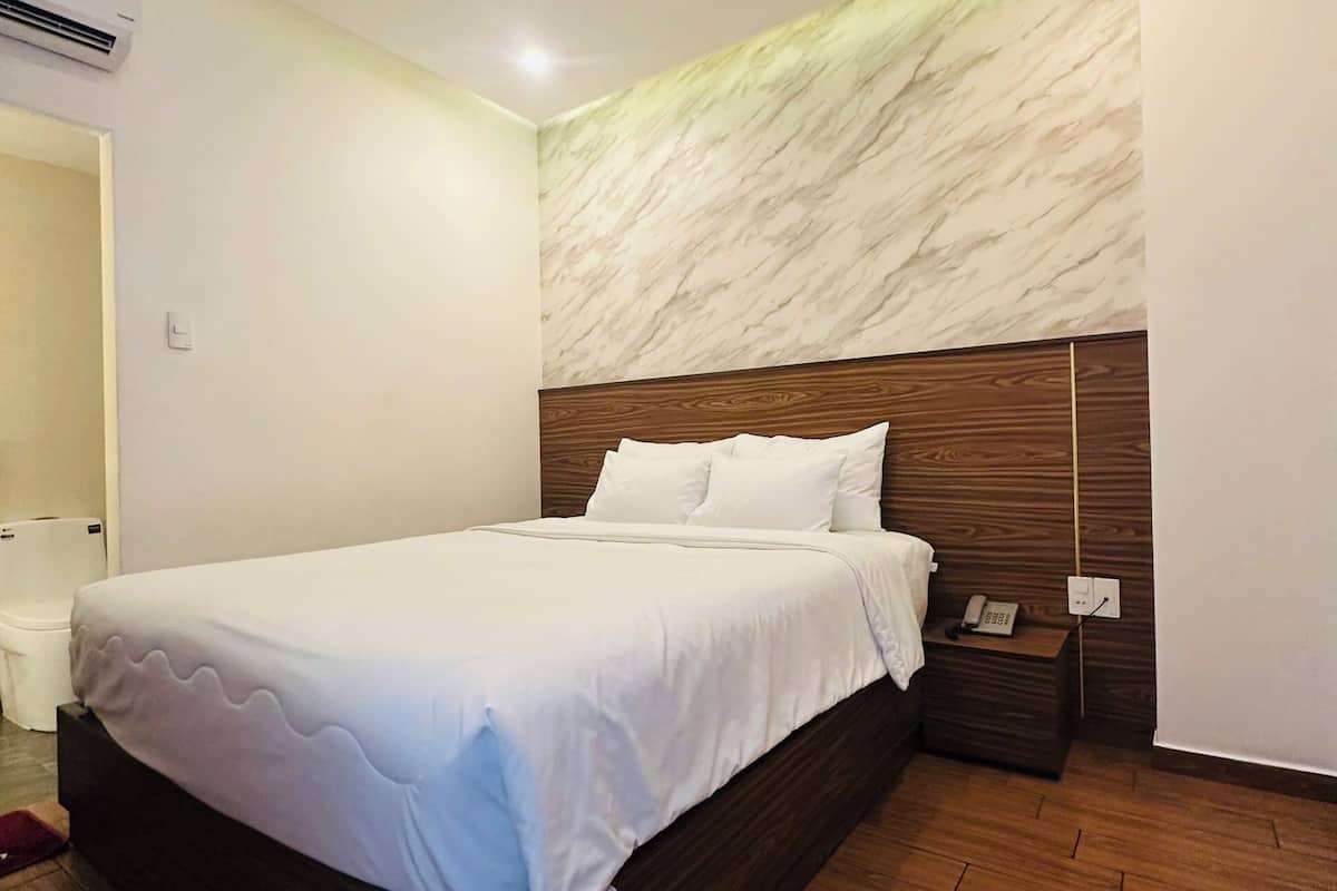 A modern hotel room with a large bed, wooden headboard, and a marble accent wall.
