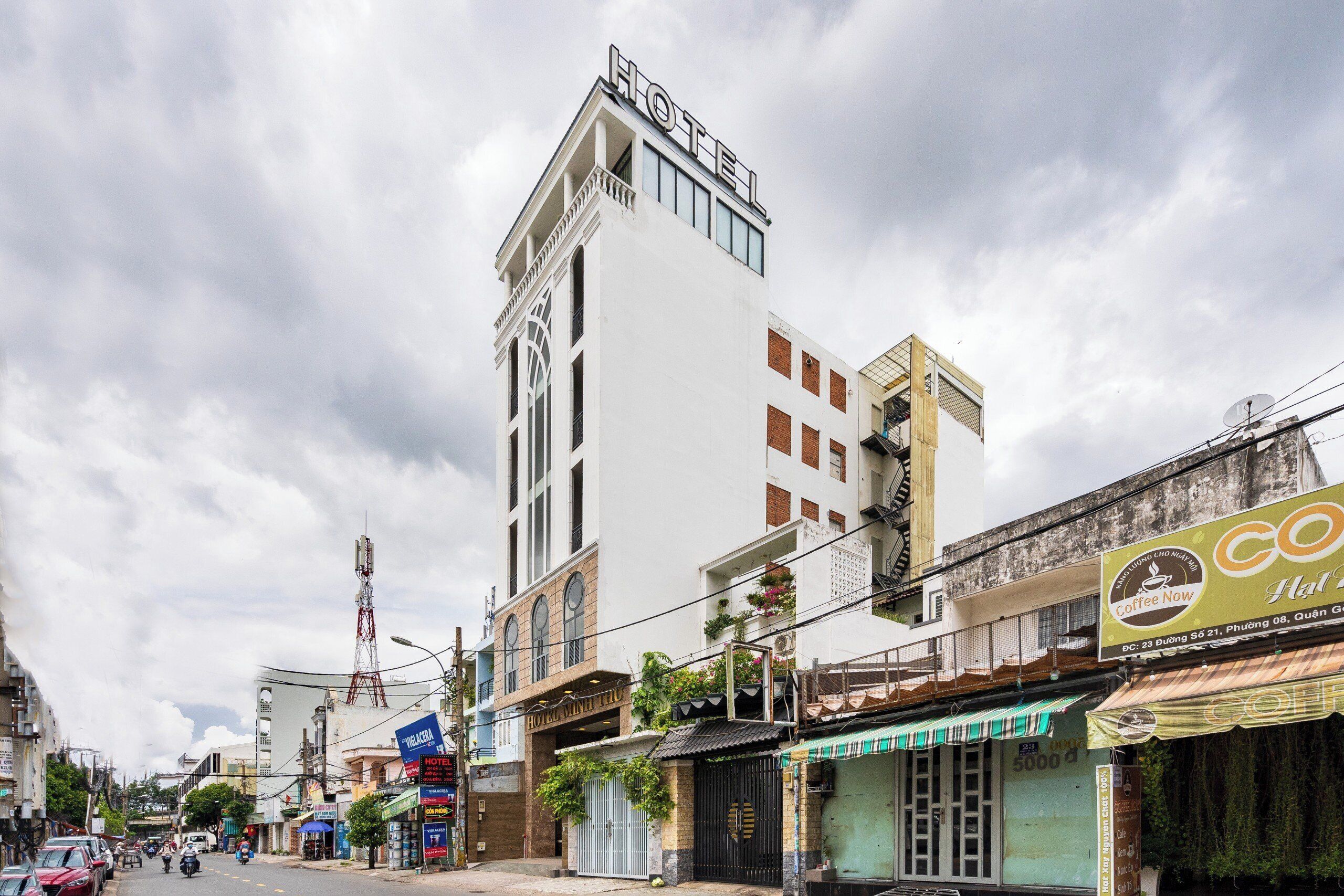 A hotel with a prominent sign, a street view with various shops, and a clear sky.