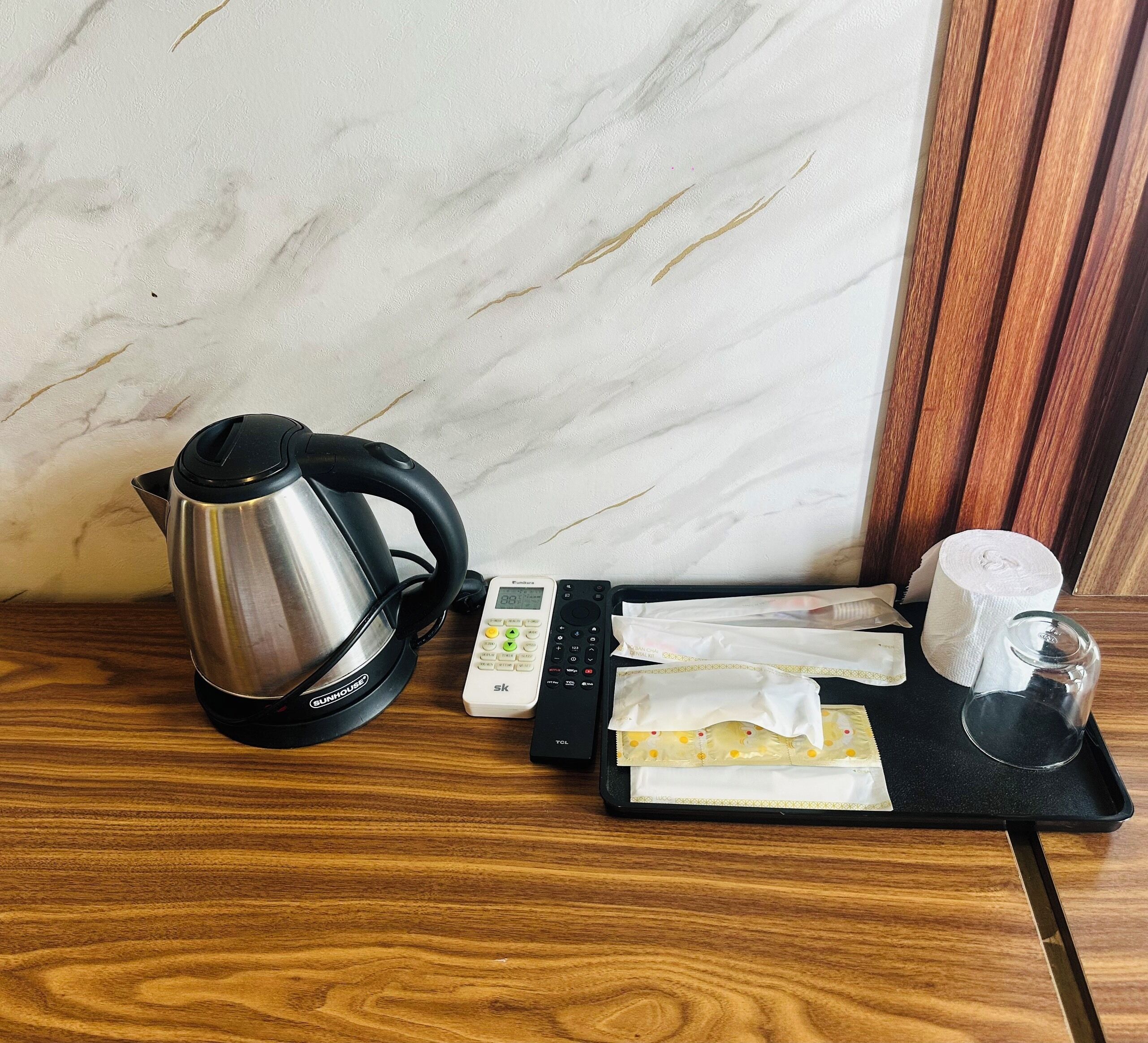 Un coin cuisine équipé d’une bouilloire en acier inoxydable, d’une machine à café numérique, d’un plateau avec un verre, des serviettes en papier et un rouleau de mouchoirs.