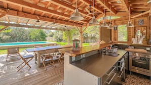 Eine Außenküche mit einer Holzterrasse, einem Pool und einem Essbereich mit Stühlen und einem Tisch.
