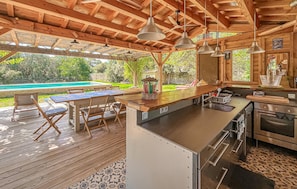 An outdoor kitchen with a wooden deck, a pool, and a dining area with chairs and a table.