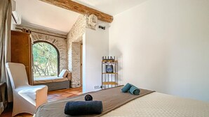 Ein Schlafzimmer mit einem Bett, einem Sessel, einem Fenster und einem an der Wand befestigten Regal.