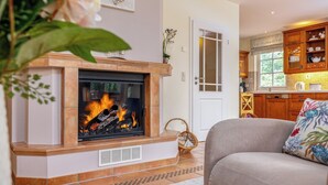 Een woonkamer met een open haard, een bank en een keukenhoek met houten kasten en een raam.