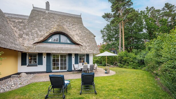 Een rieten huis met een patio, terrasmeubels en een tuin.