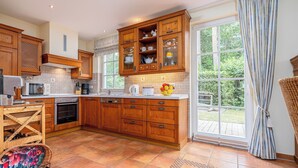 Een keuken met houten kastjes, een betegelde spatwand en een groot raam met gordijnen.
