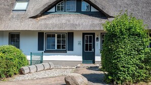 Une maison traditionnelle à toit de chaume, avec une porte verte, des murs blancs et un chemin de gravier menant à l’entrée.