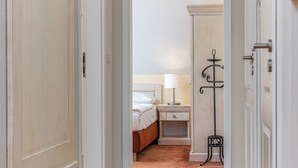 Un couloir étroit mène à une chambre à coucher qui contient un lit, une table de chevet, une lampe et un petit tabouret.
