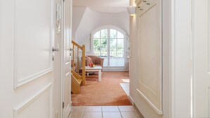 Un couloir avec un escalier menant à une pièce dotée d’une grande fenêtre en arc de cercle et d’une porte blanche.