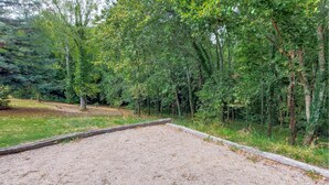 Un área de grava con un cerco de madera, rodeada de follaje verde exuberante y árboles.