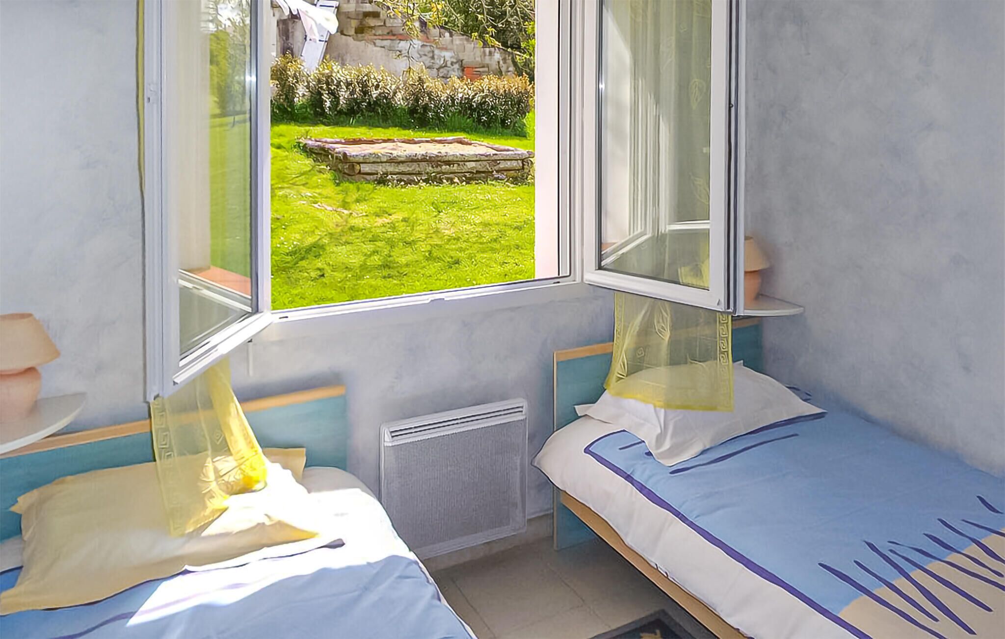 Una habitación pequeña y luminosa con dos camas, una ventana que da a un jardín y un radiador.