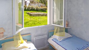 Una habitación pequeña y luminosa con dos camas, una ventana que da a un jardín y un radiador.