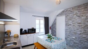 A compact kitchen with a microwave, kettle, and sink. A small dining table with a bench is in the center.