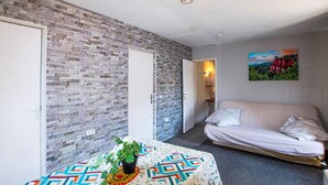 A bedroom with a patterned bedspread, a potted plant, a white sofa, and a painting on the wall.