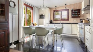 A modern kitchen with white cabinets, a dining table with chairs, a chandelier, and a window with blinds. - Amazing home in Erm with WiFi (Erm)