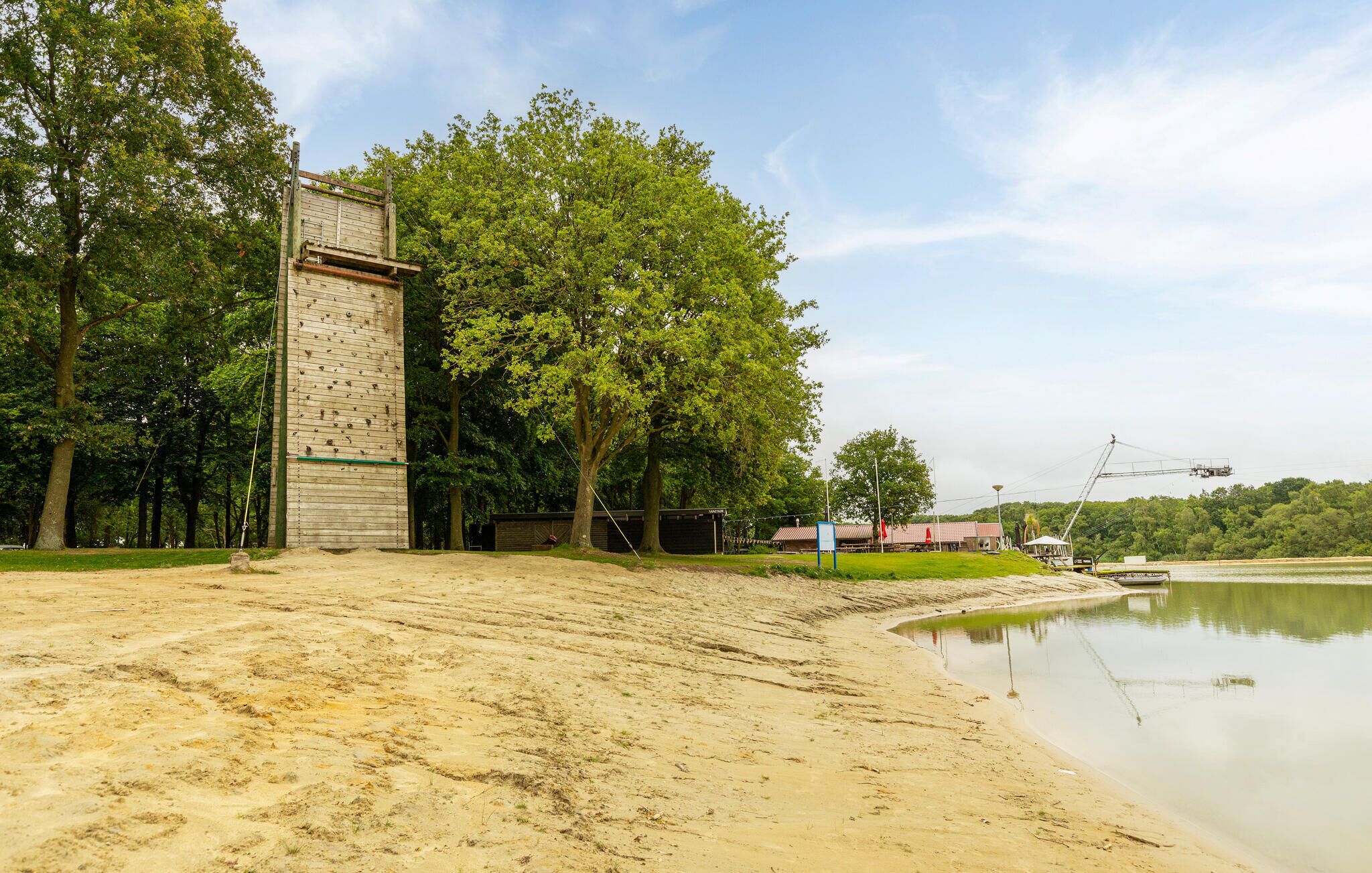 A sandy beach area with a large wooden structure, possibly a boathouse, near a calm body of water.