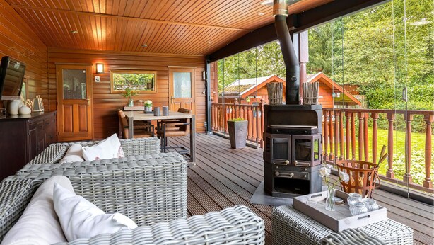 A cozy wooden deck with wicker furniture, a fireplace, and a view of the surrounding forest.