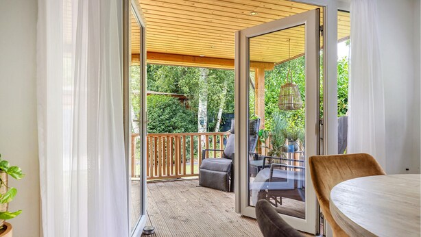 An open sliding glass door leading to an outdoor deck with a wooden ceiling, a table, chairs, and a hanging light fixture. - 1 bedroom stunning home in Erm (Erm)
